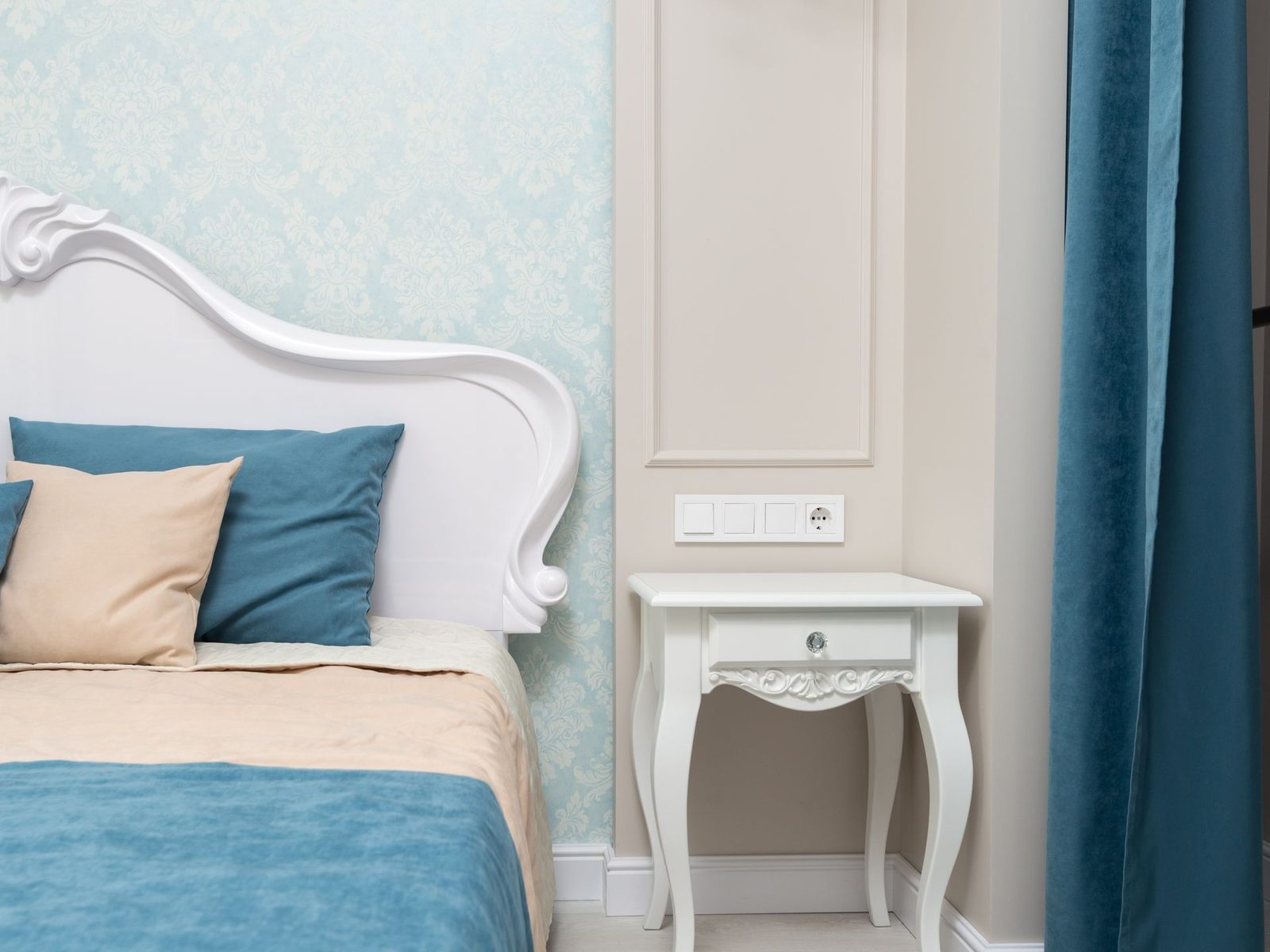 Classic bedroom corner with a soft blue damask wallpaper, carved white headboard, and teal velvet drapery