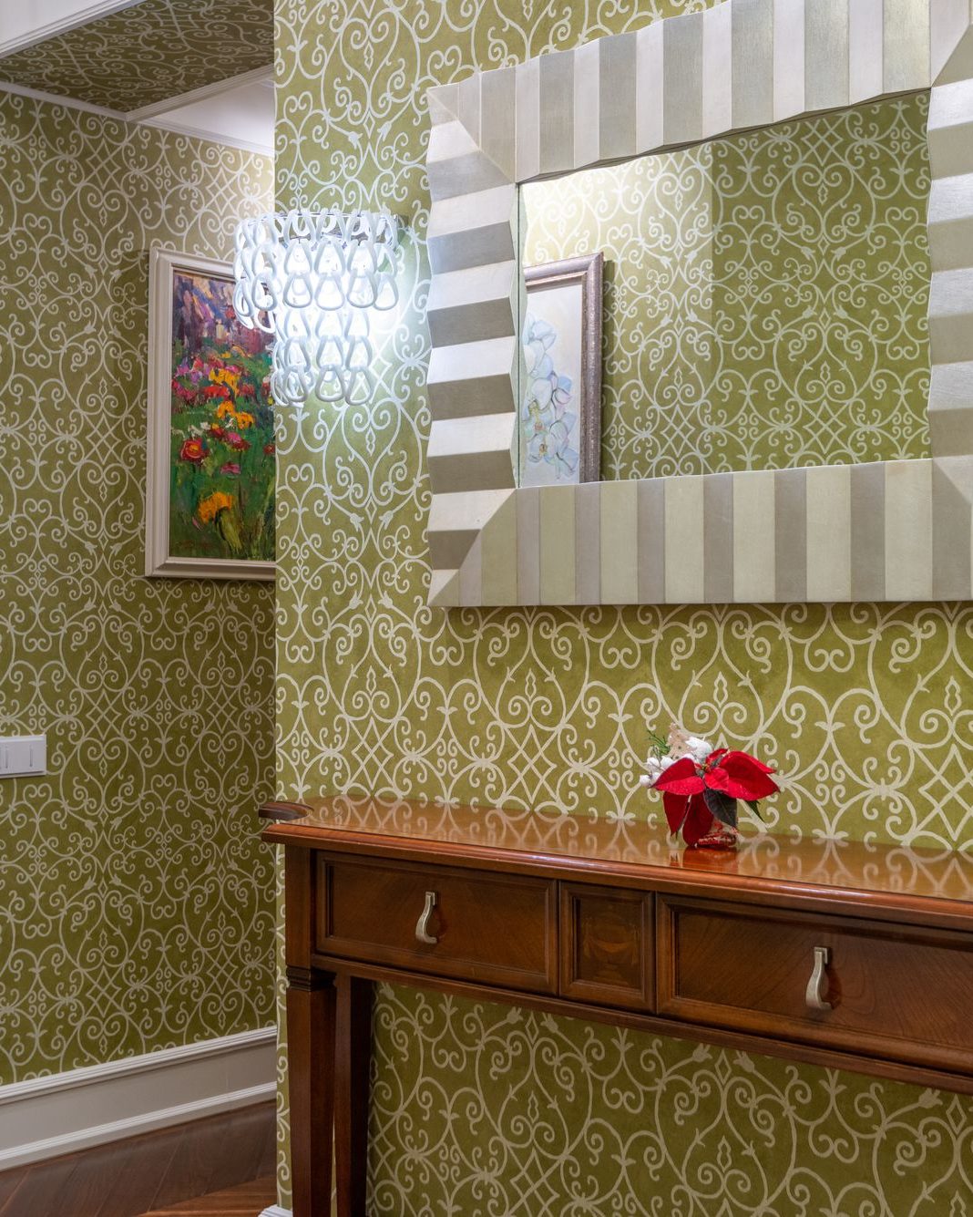 Elegant entry hallway finished in a scrolled olive vine-and-trellis wallpaper, with a framed mirror and wood console table