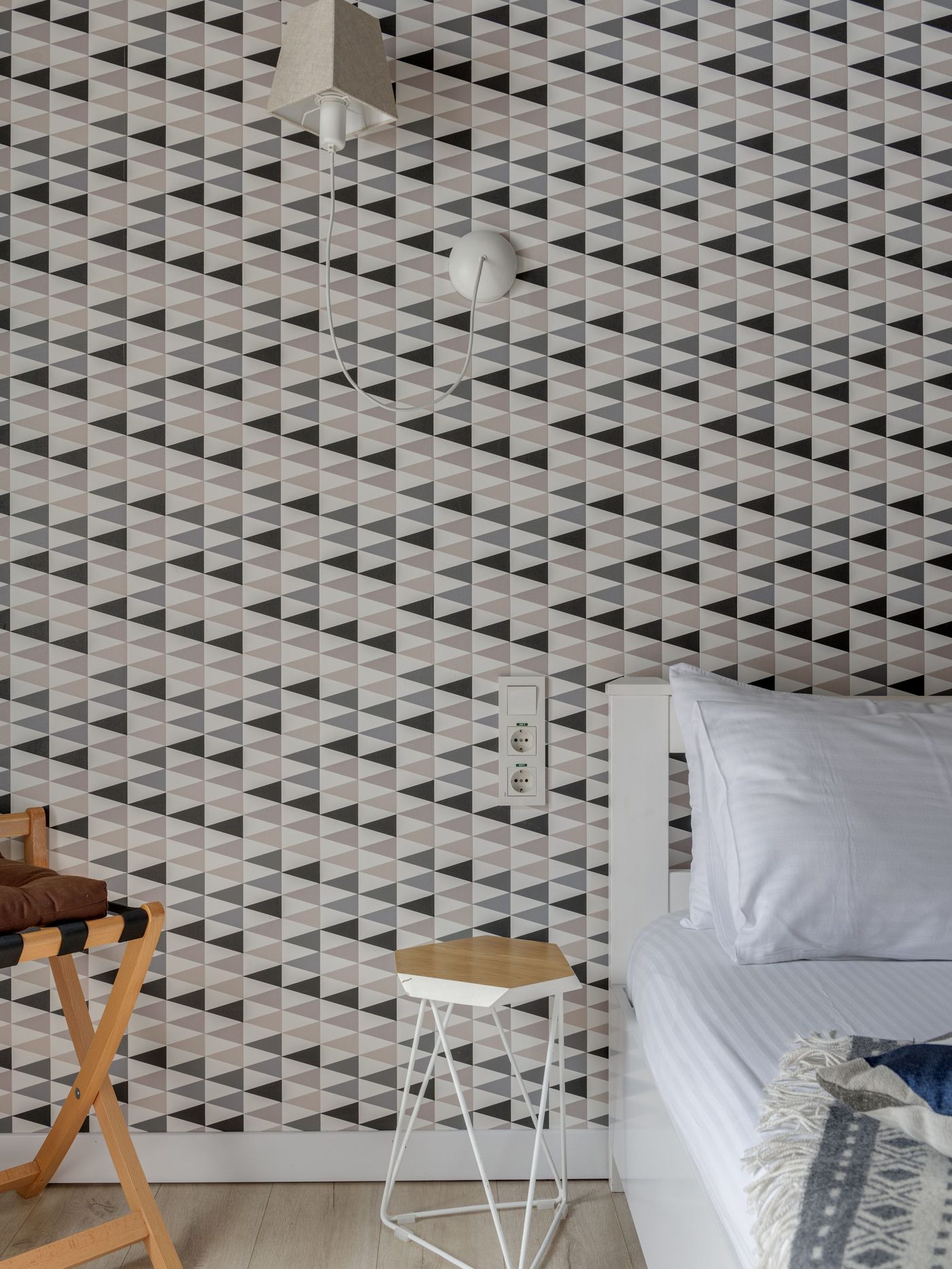 Close-up of a precisely hung geometric triangle-pattern wallpaper beside a neatly dressed bed, showing crisp seam alignment